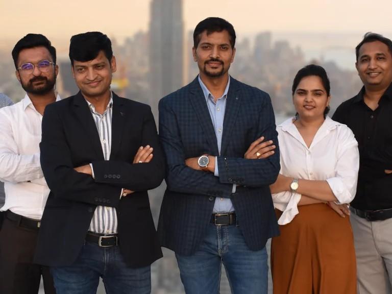 Five members of the team standing in a row, some with their arms crossed, a city skyline behind them at sunset