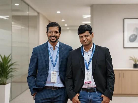 Two colleagues standing side by side in a bright office corridor, both wearing lanyards