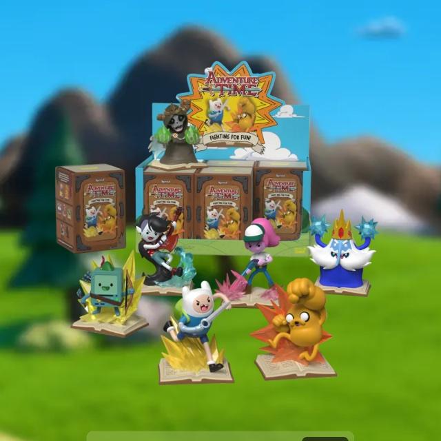 Kwistal Adventure Time Fighting for Fun collectible figures of Finn, Jake, Ice King and others in front of a display box, on a blurred green landscape