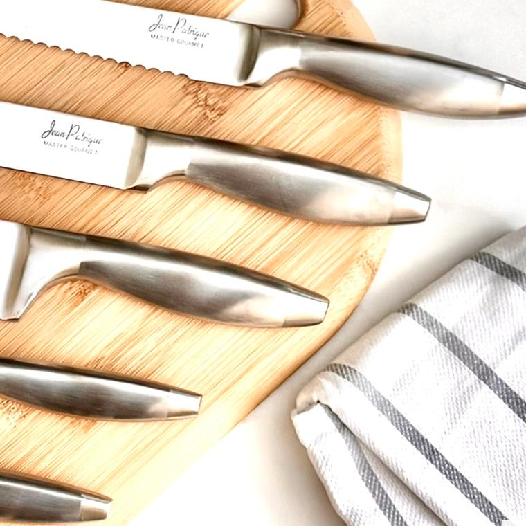 Brushed steel handles of Jean Patrique Master Gourmet knives on a bamboo board beside a striped kitchen towel