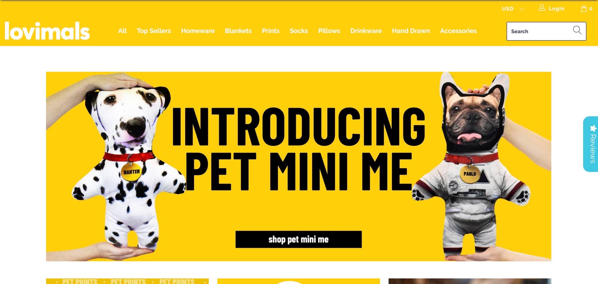 Lovimals home page on a yellow background with the menu All, Top Sellers, Homeware, Blankets, Prints, Socks, Pillows, Drinkware, Hand Drawn and Accessories, and a banner Introducing Pet Mini Me with a plush Dalmatian and a plush French bulldog in an astronaut suit